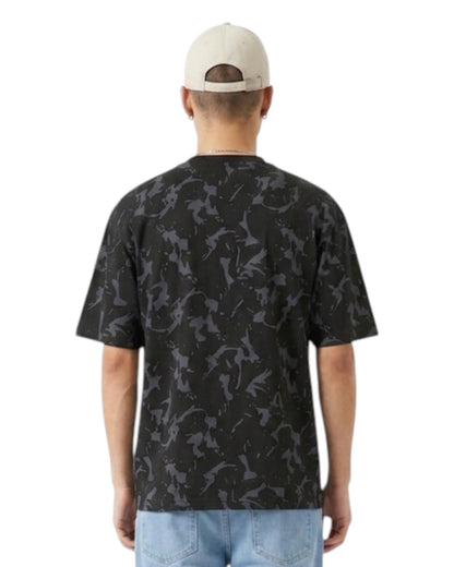 Anetos Blackout Camo Tee: Men's black t-shirt with grey camouflage print, short sleeves, and relaxed fit. Model wears light wash jeans and a beige cap.