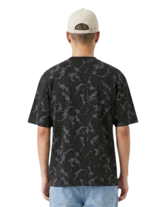 Anetos Blackout Camo Tee: Men's black t-shirt with grey camouflage print, short sleeves, and relaxed fit. Model wears light wash jeans and a beige cap.