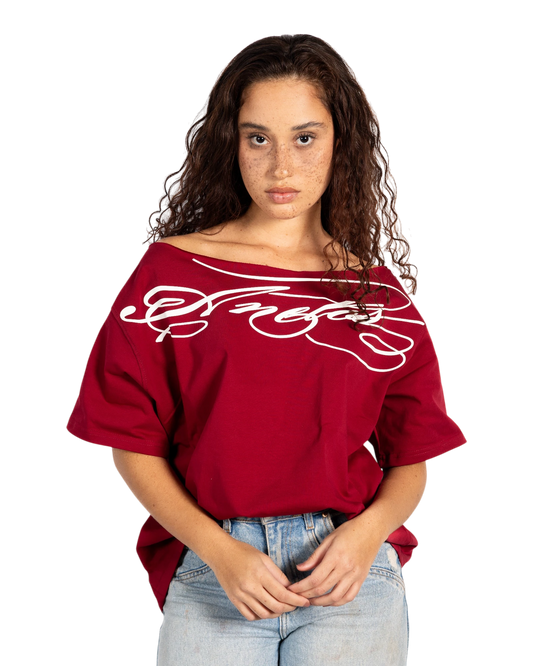 Anetos burgundy off-shoulder t-shirt with white graphic print and cuffed sleeves, paired with denim jeans.